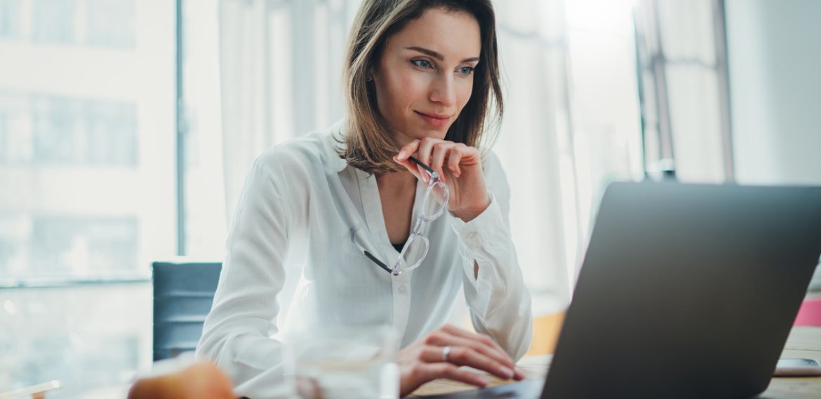 Confident businesswoman working on laptop at her workplace at modern office.Blurred background.
